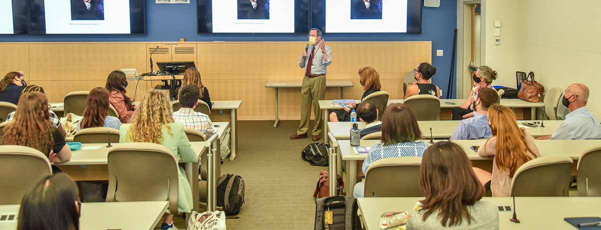 Students facing the front of a classroom as a professor teaches.
